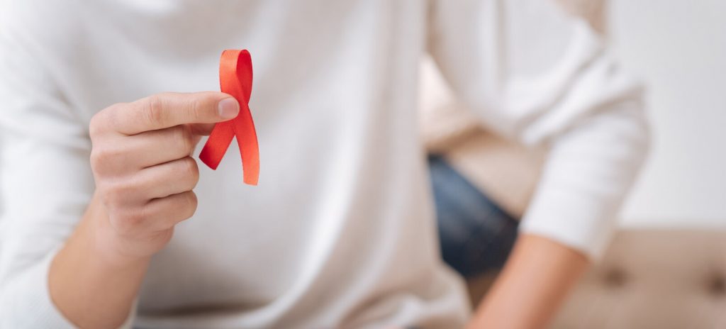 Man houdt een rood lintje vast: het symbool van hiv-aids