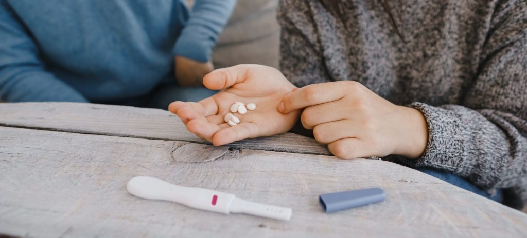 Vrouw heeft een paar pillen in haar hand en er ligt een zwangerschapstest op tafel