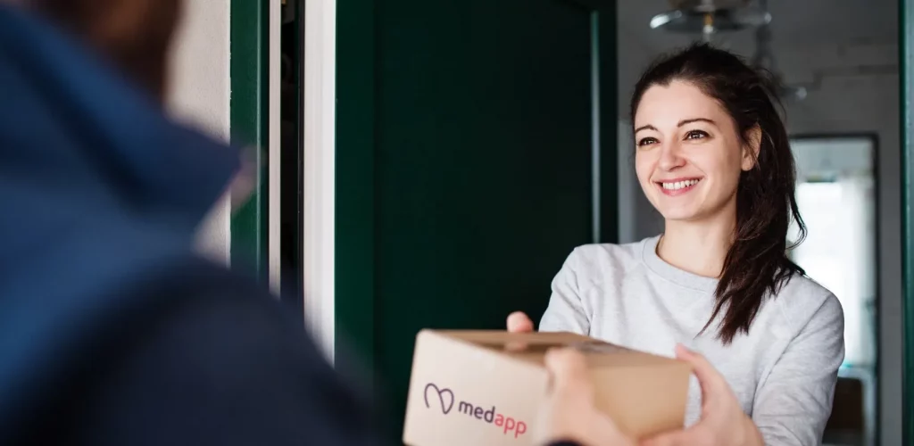 Lachende jonge vrouw ontvangt een pakketje van MedApp aan de deur