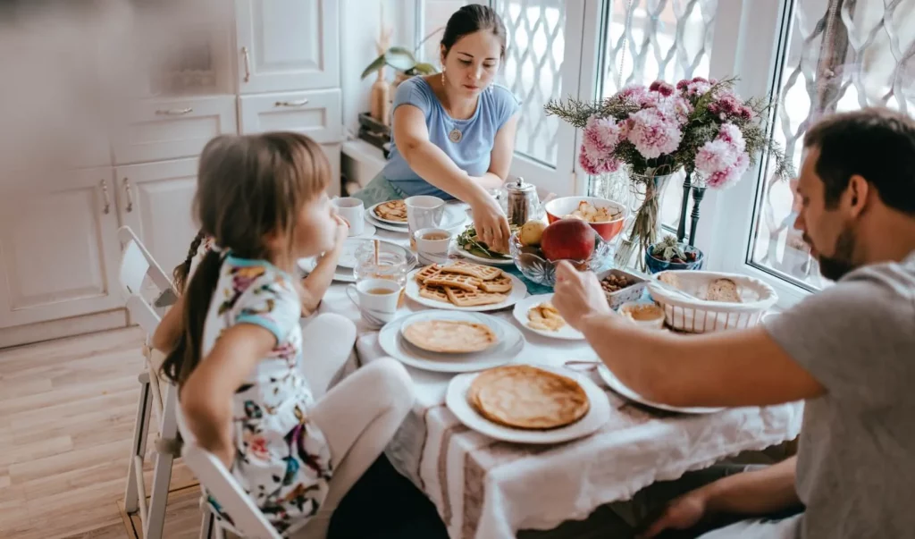 Jonge man en vrouw eten pannenkoeken aan de ontbijttafel samen met hun twee kinderen