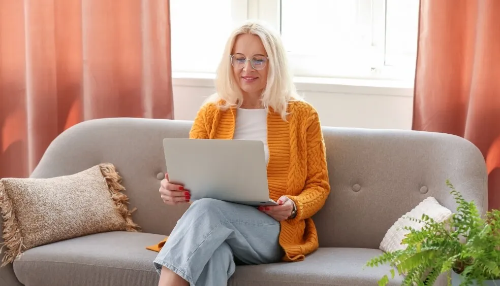 Blonde vrouw zit op de bank en bekijkt de website van MedApp op haar laptop