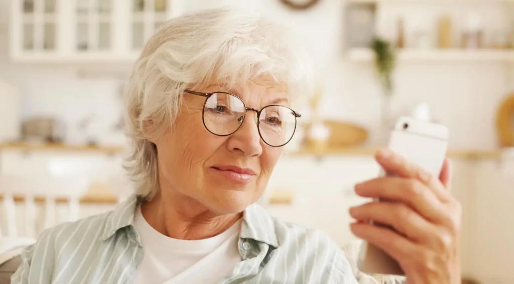 Oudere vrouw in witgestreepte blouse houdt haar mobieltje vast en leest aandachtig de tekst
