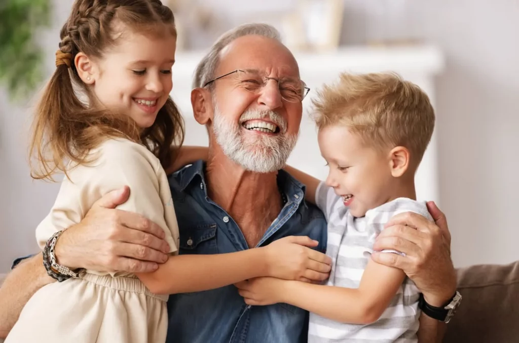 Oude man lacht met ogen dicht terwijl hij zijn twee kleinkinderen vasthoudt