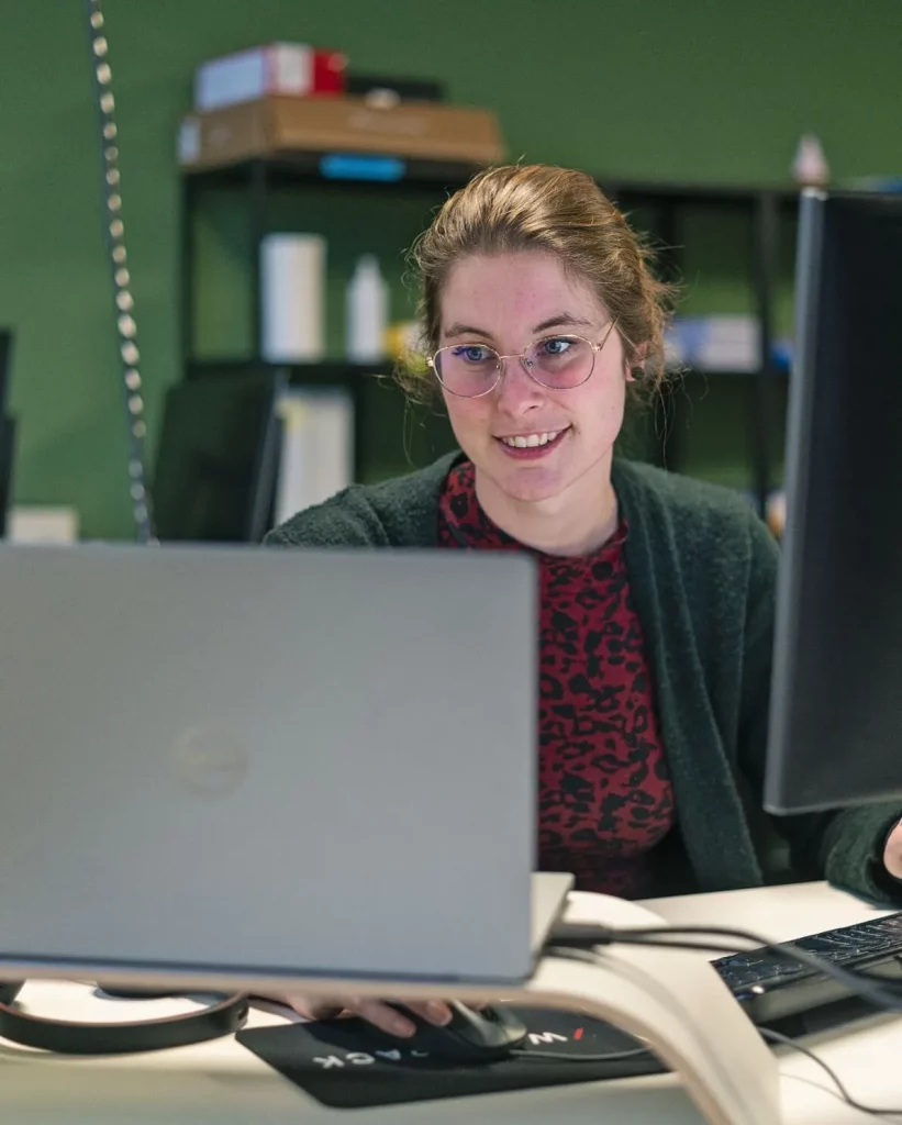 Medewerkster Tika zit glimlachend achter twee computerschermen