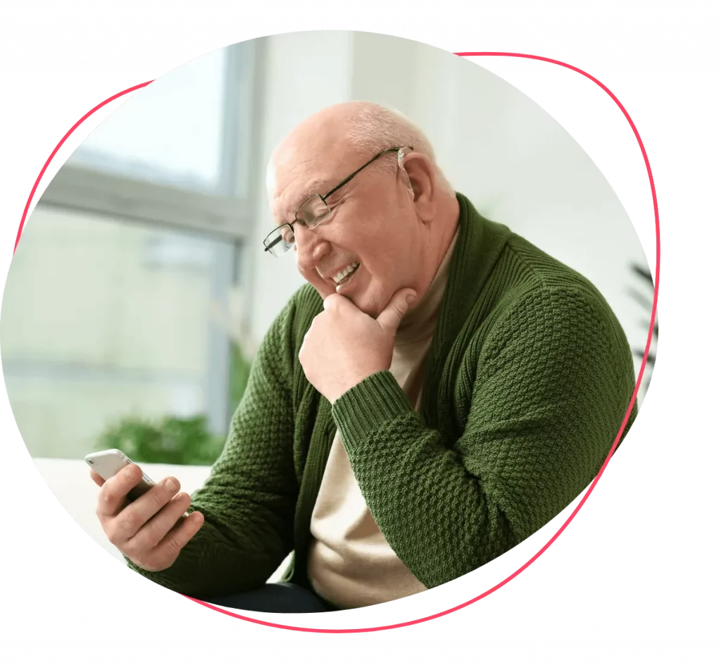 Oudere man met groen vest kijkt lachend naar de mobiele telefoon in zijn rechterhand