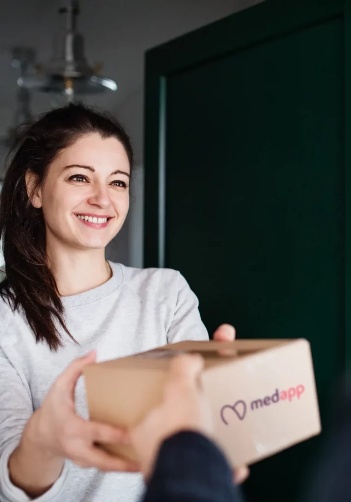 Lachende jonge vrouw ontvangt een pakketje van MedApp aan de deur