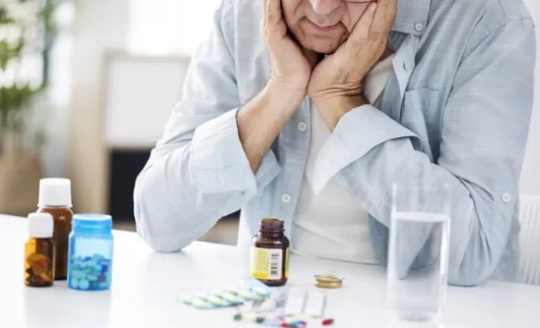 Bejaarde man zit aan tafel en kijkt naar zijn voorraad medicijnen
