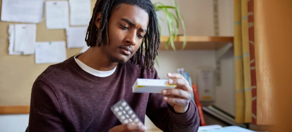 jonge student zit aan zijn bureau en kijkt aandachtig naar een doosje met pillen
