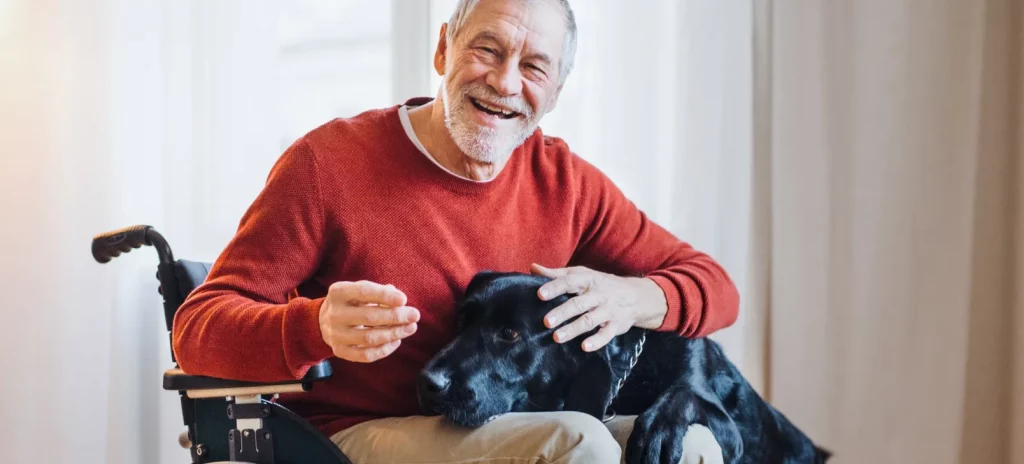 oude man zit lachend in een rolstoel en knuffelt een zwarte hond