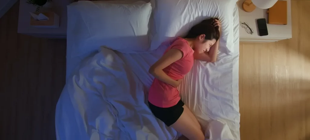 jonge vrouw ligt 's nachts op bed en heeft haar hand op haar buik vanwege maagpijn