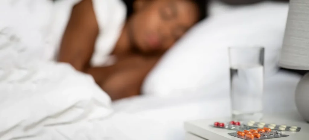jonge vrouw ligt in bed en er liggen pillen naast haar op het nachtkastje